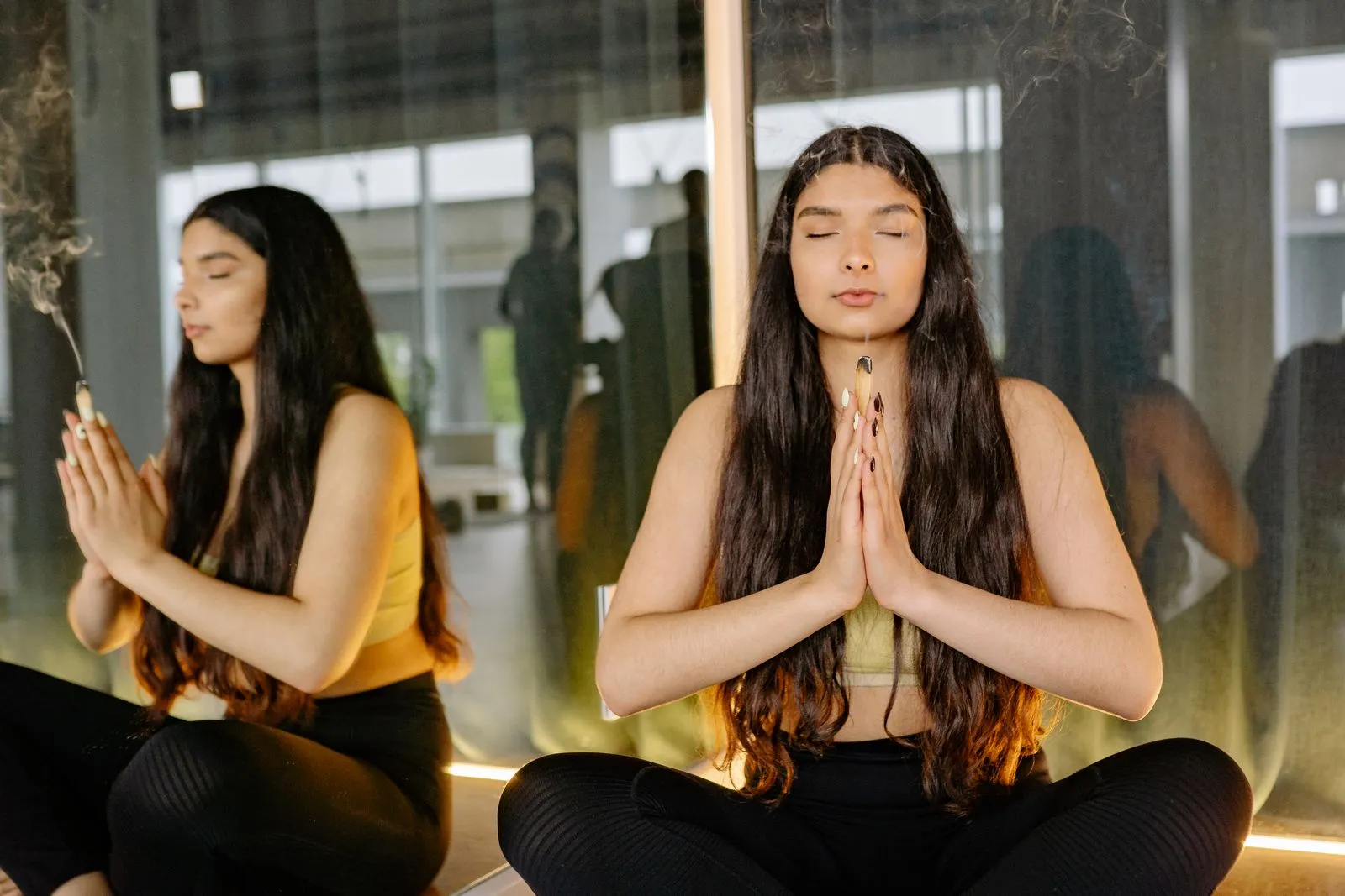 Woman practicing meditation with incense, reflecting peaceful wellness in a serene yoga studio setting.
